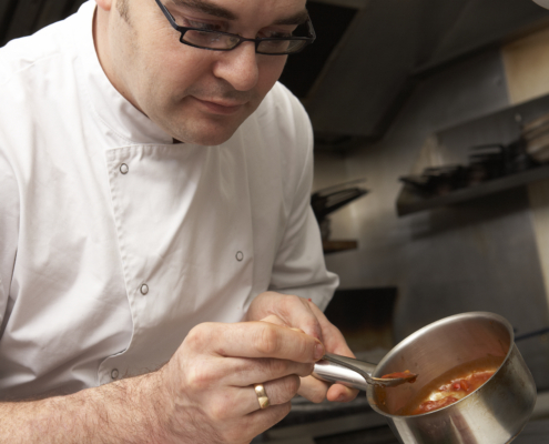 Chef Adding Sauce To Dish In Restaurant Kitchen