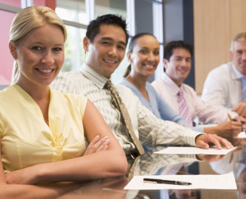 Five businesspeople at boardroom table smiling
